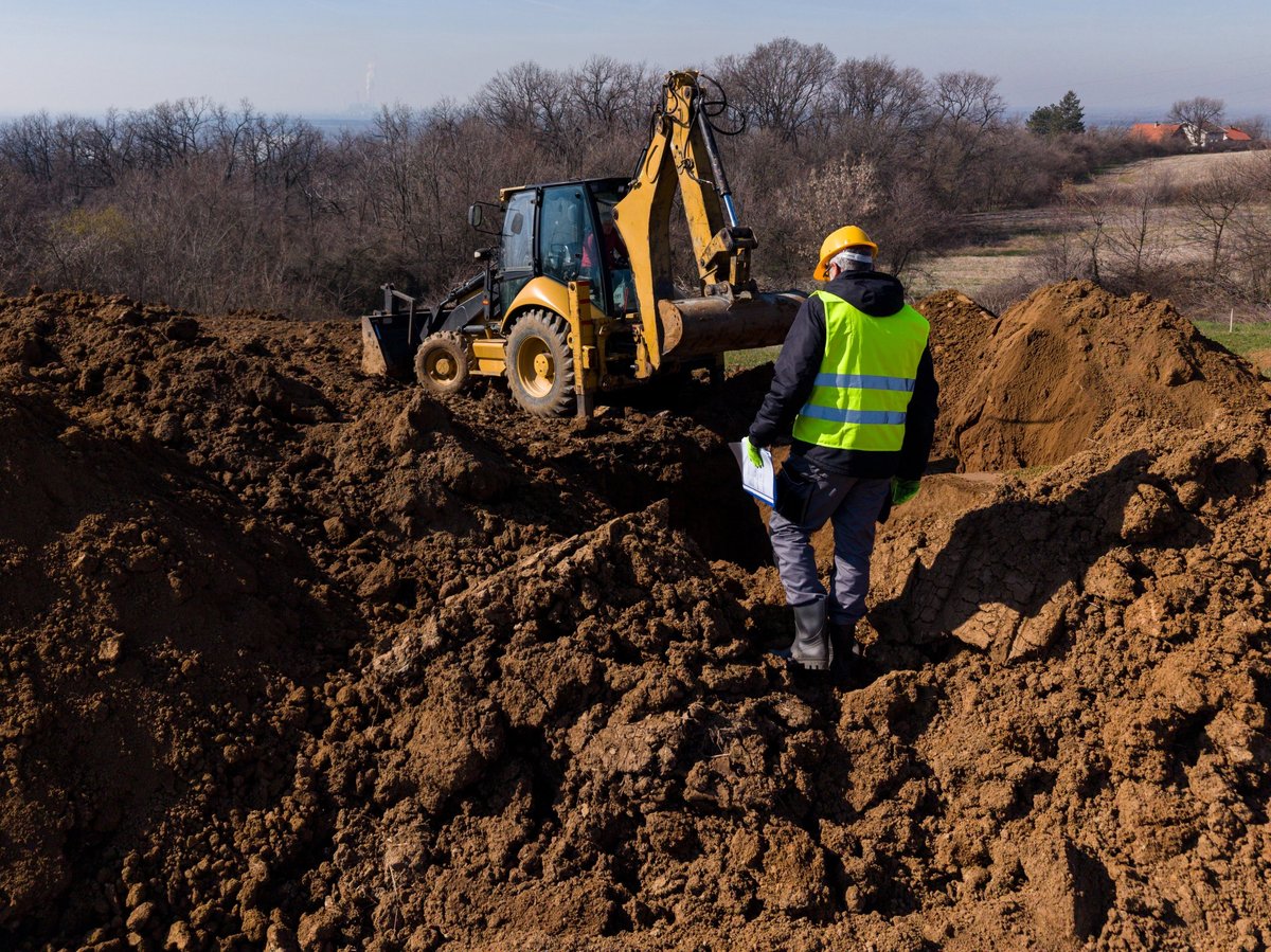Bauleiter auf Erdbau-Baustelle mit Bagger bei Aushubarbeiten