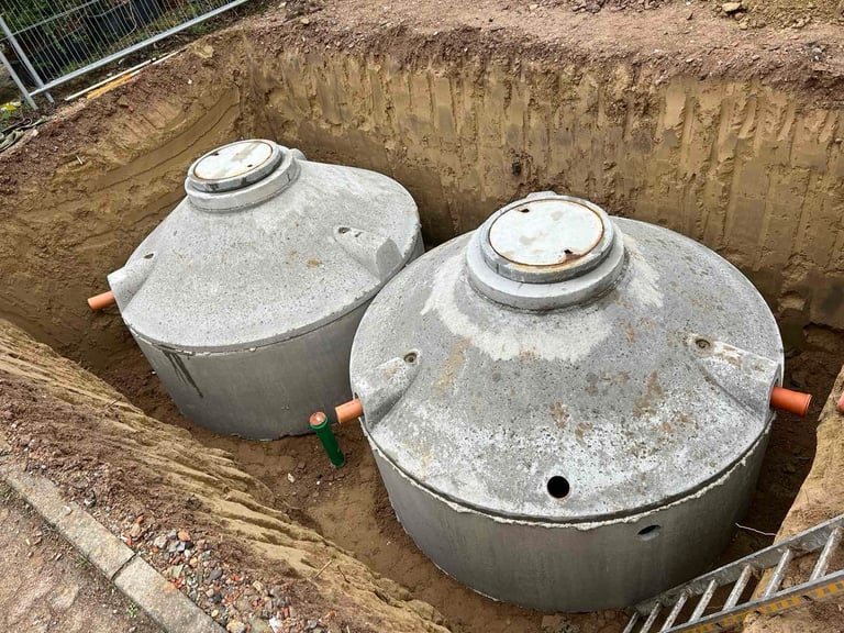Two large concrete septic tanks installed in an excavated pit with metal access covers and copper piping.
