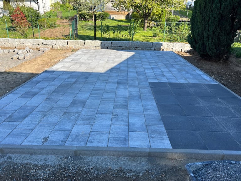 New blue and gray paver patio in residential backyard with landscaping and trees in background