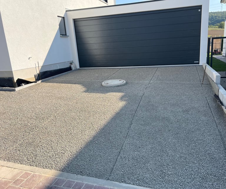 Modern driveway with black garage door, split into light gravel and dark asphalt sections with white trim