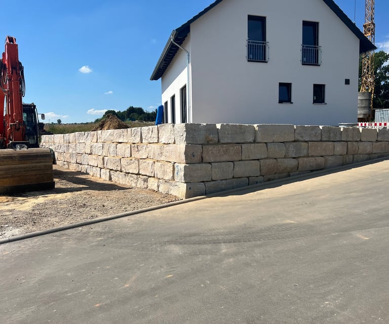 Modern white house with stone retaining wall and paved driveway under clear blue sky